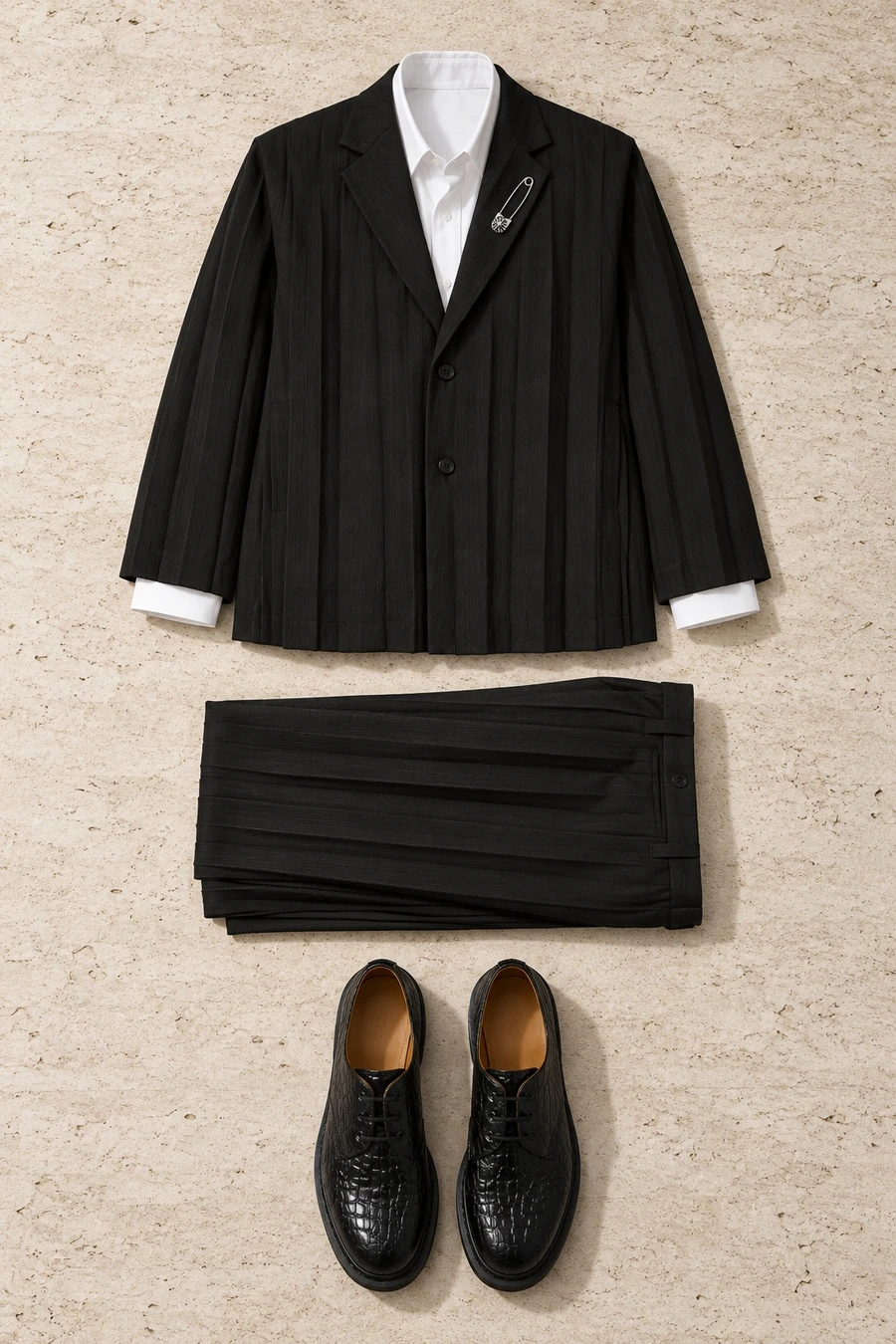 A pleated black suit for a winter wedding. Flat lay of a black Issey Miyake jacket, black trousers, a white COOR shirt and black Dr. Martens derbies.
