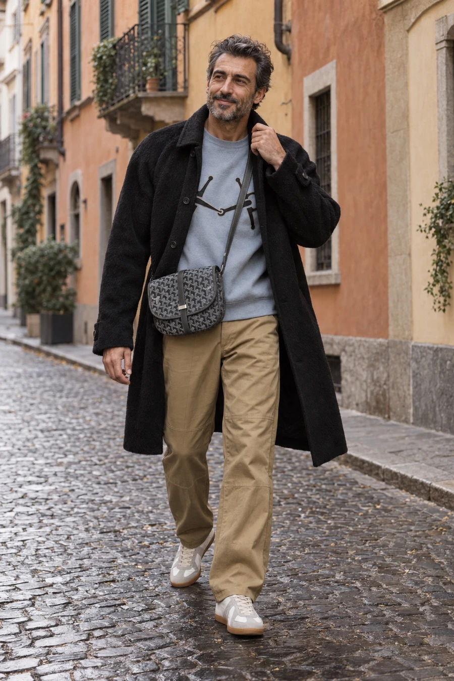 An Italian man in a black alpaca coat, a pale blue Hermès crewneck, khaki Helmut Lang trousers and Margiela sneakers walks through Brera with a Goyard bag.