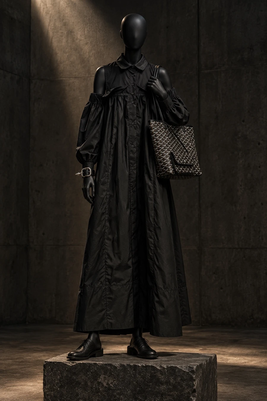 A black display mannequin in a Giovanni Cavagna shirt dress with full sleeves, Guidi mules, a Goyard tote and a Chrome Hearts bracelet, on a plinth in a concrete gallery.
