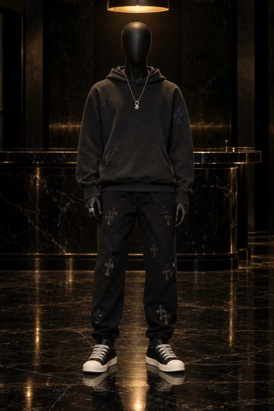A faceless black mannequin wears a Chrome Hearts hoodie, cross patch sweatpants, Rick Owens Ramones, a Gunslinger ring and a ball chain in a dark bar room.