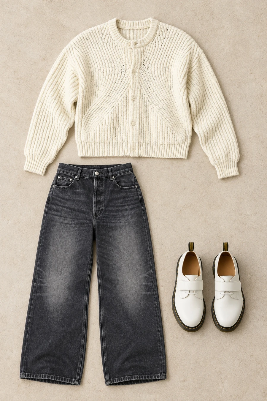 An overhead flatlay of a cream COOR cardigan, washed black A.P.C. jeans and white Dr. Martens shoes with straps.