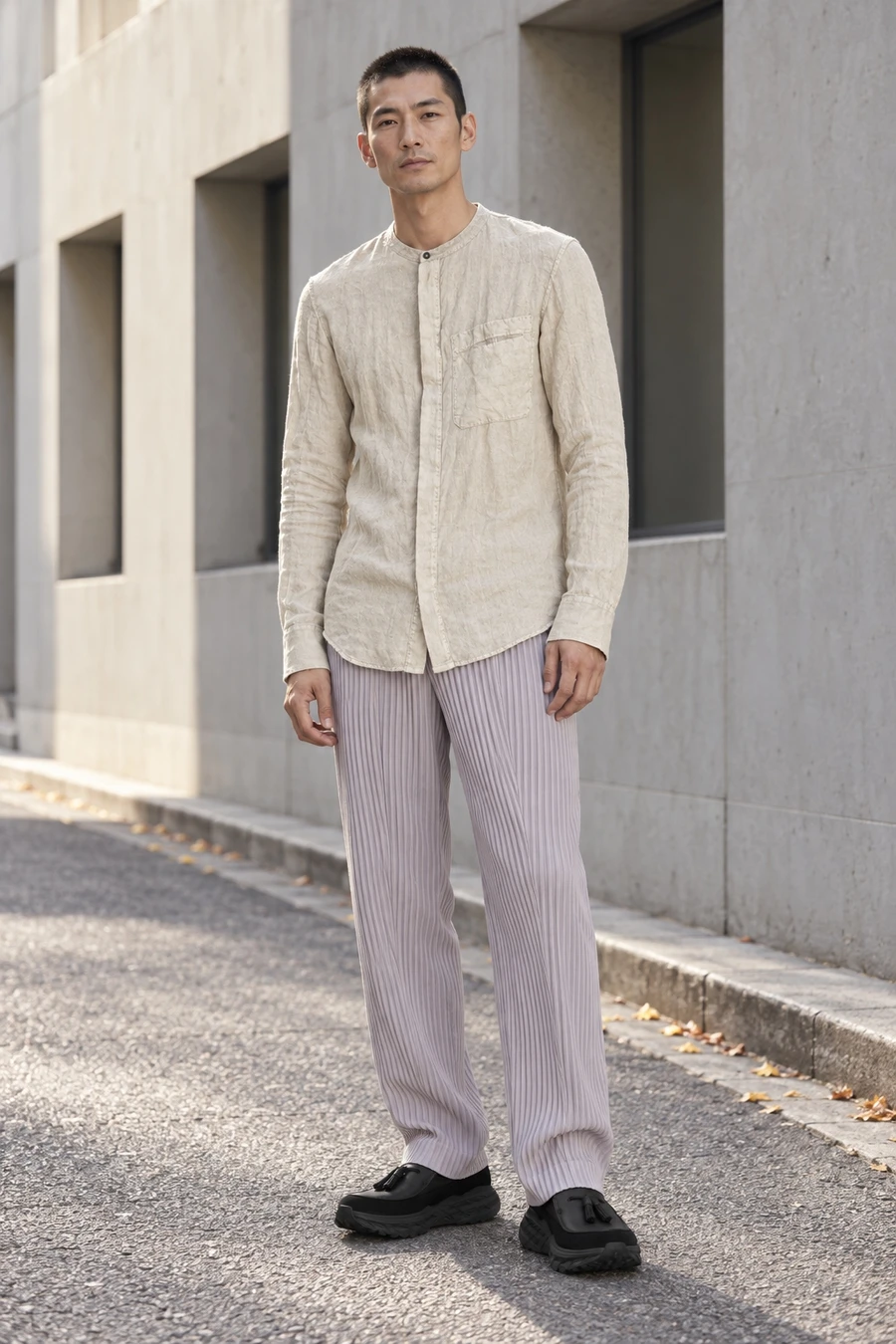 An adult man wears a pale band collar shirt, light purple pleated trousers and black tassel loafers on a Tokyo street.