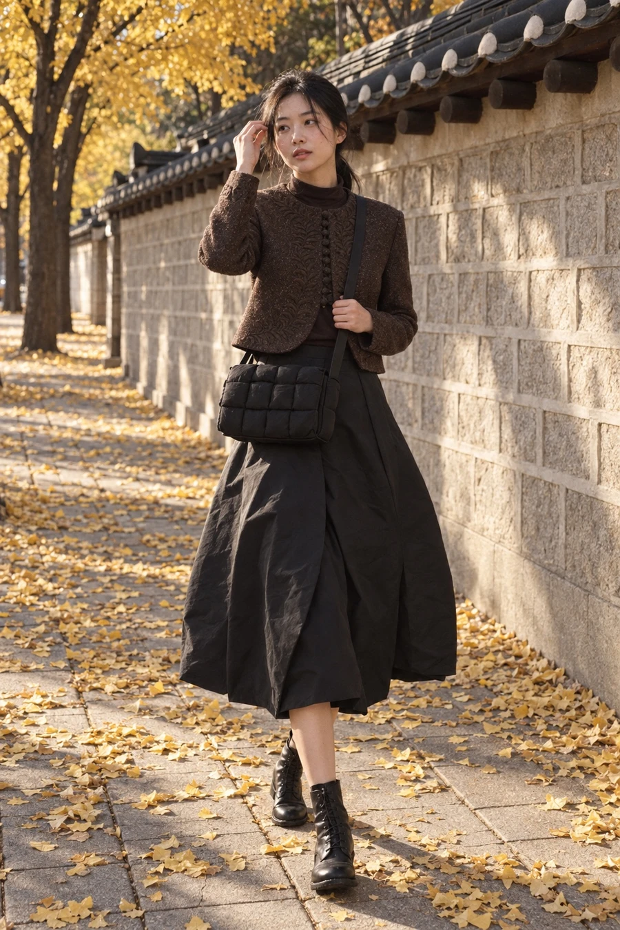A Korean woman in a brown INTO THE EAST tweed jacket, a chocolate turtleneck, a black Litkovska balloon skirt and black Guidi lace up boots walks under yellow ginkgo trees in Seoul with a Bottega Veneta Cassette.