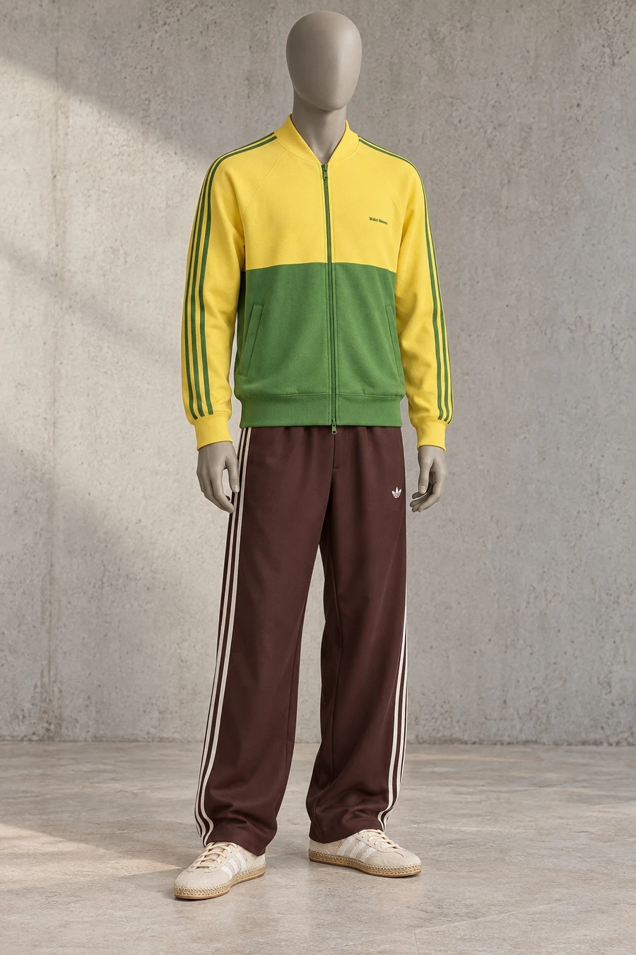 A faceless grey mannequin wears a gold and green track jacket, wide brown track trousers and cream woven trainers.