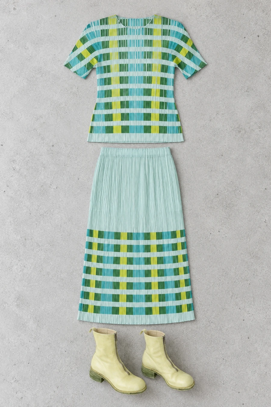 A flatlay of a mint and green checked Pleats Please top and skirt with a pair of pale kiwi Guidi boots.