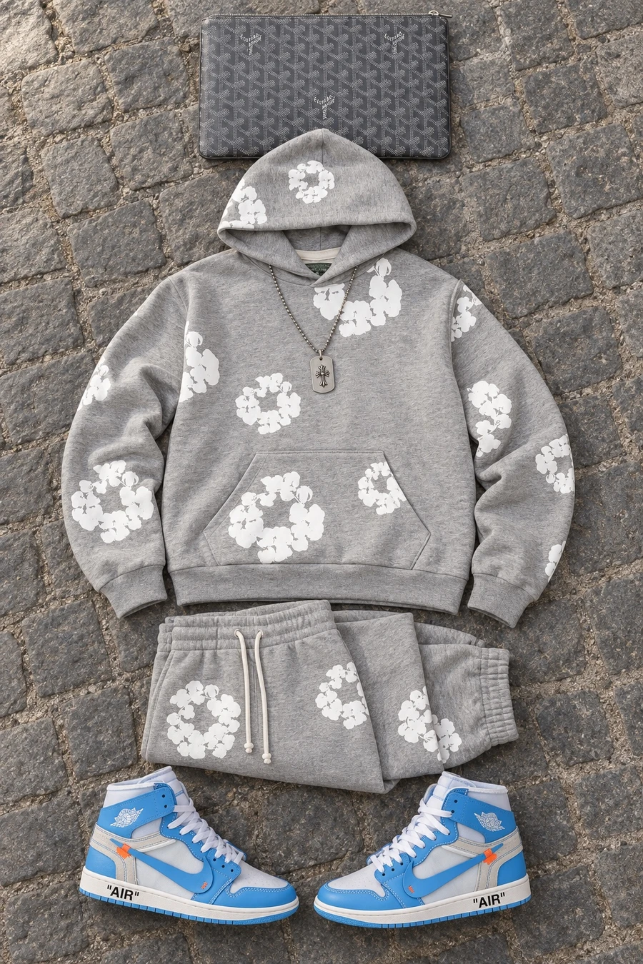 Outside the shows in Paris. Flat lay of a grey Denim Tears sweatshirt, grey track pants, blue Jordan sneakers and a grey Goyard pouch.