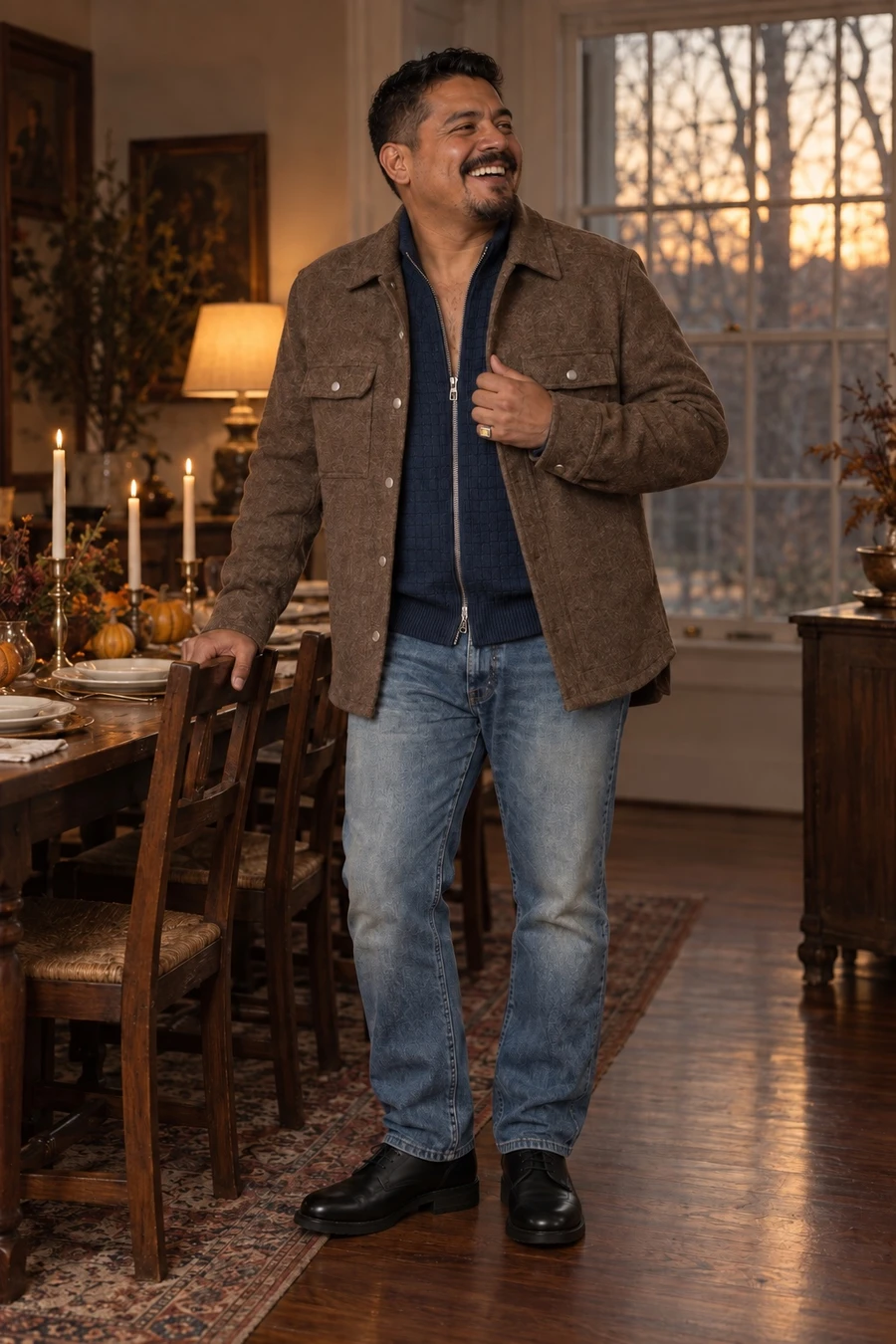 A Mexican American man in a fawn Rick Owens overshirt, a navy Louis Vuitton cardigan, light Kapital jeans and black Guidi derbies laughs at the end of a Thanksgiving table.