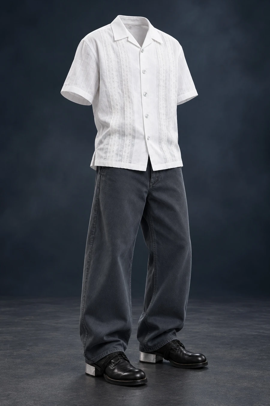 White woven panels run down a COOR shirt above curved charcoal trousers and Guidi shoes with metal heels. The complete outfit stands against a dark studio background.